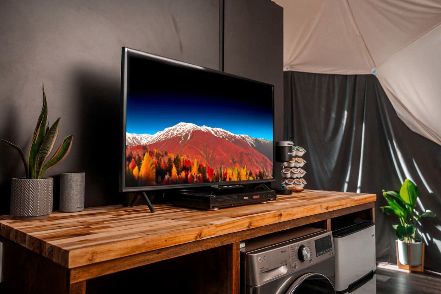 Un téléviseur à écran plat posé sur un meuble télé en bois, un lave-linge et une pile de tasses à café.