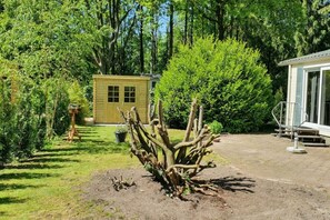 Ein Garten mit einer Holzhütte, einem Busch und einem Gebäude mit einer Veranda.