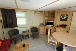 Ein gemütlicher Wohnbereich mit Sofa, zwei Sesseln, einem kleinen Tisch, einem Esstisch, einem Fernseher und einem Bücherregal.