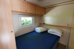 Ein kleiner Wohnmobil mit Einzelbett, einem Fenster, Holzschränken und einer einfachen Schlafgelegenheit.