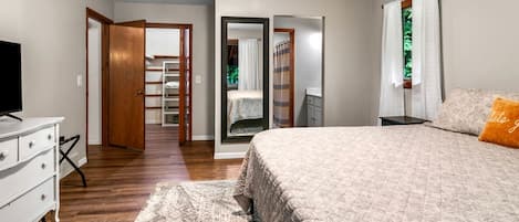 A bedroom with a bed, a dresser, a television, and a walk-in closet.