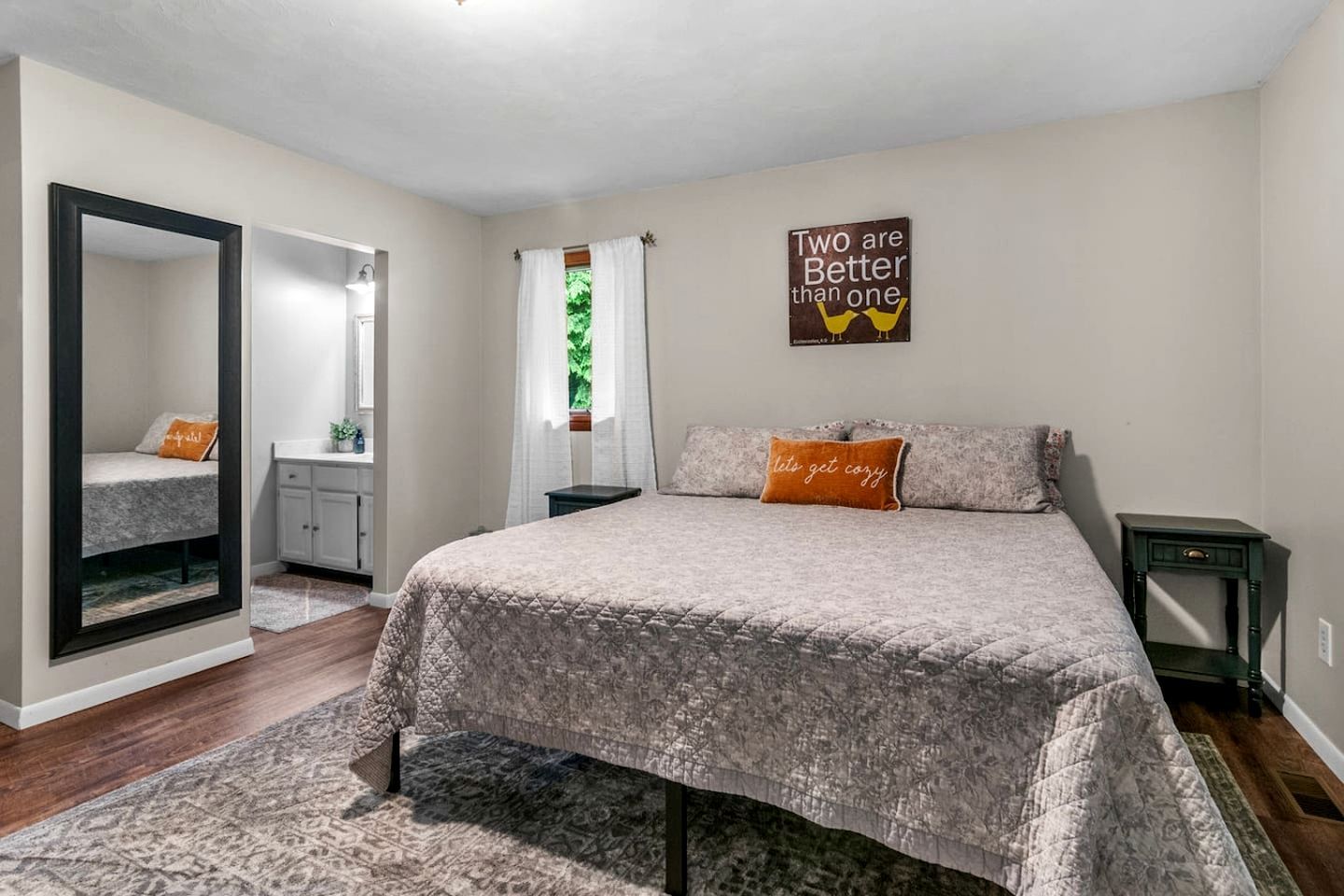A bedroom with a bed, a nightstand, a dresser, a mirror, and a window with curtains.