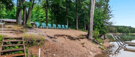 A sandy beach area with wooden steps leading down to the water, surrounded by trees and a row of green chairs.