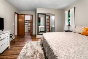 Ein Schlafzimmer mit Bett, Kommode, Fernseher und begehbarem Kleiderschrank.