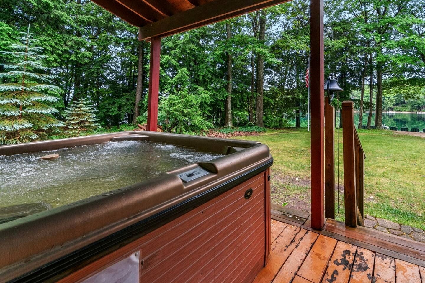 Ein Whirlpool mit einer Holzterrasse und einer Pergola, umgeben von bewaldetem Gelände.