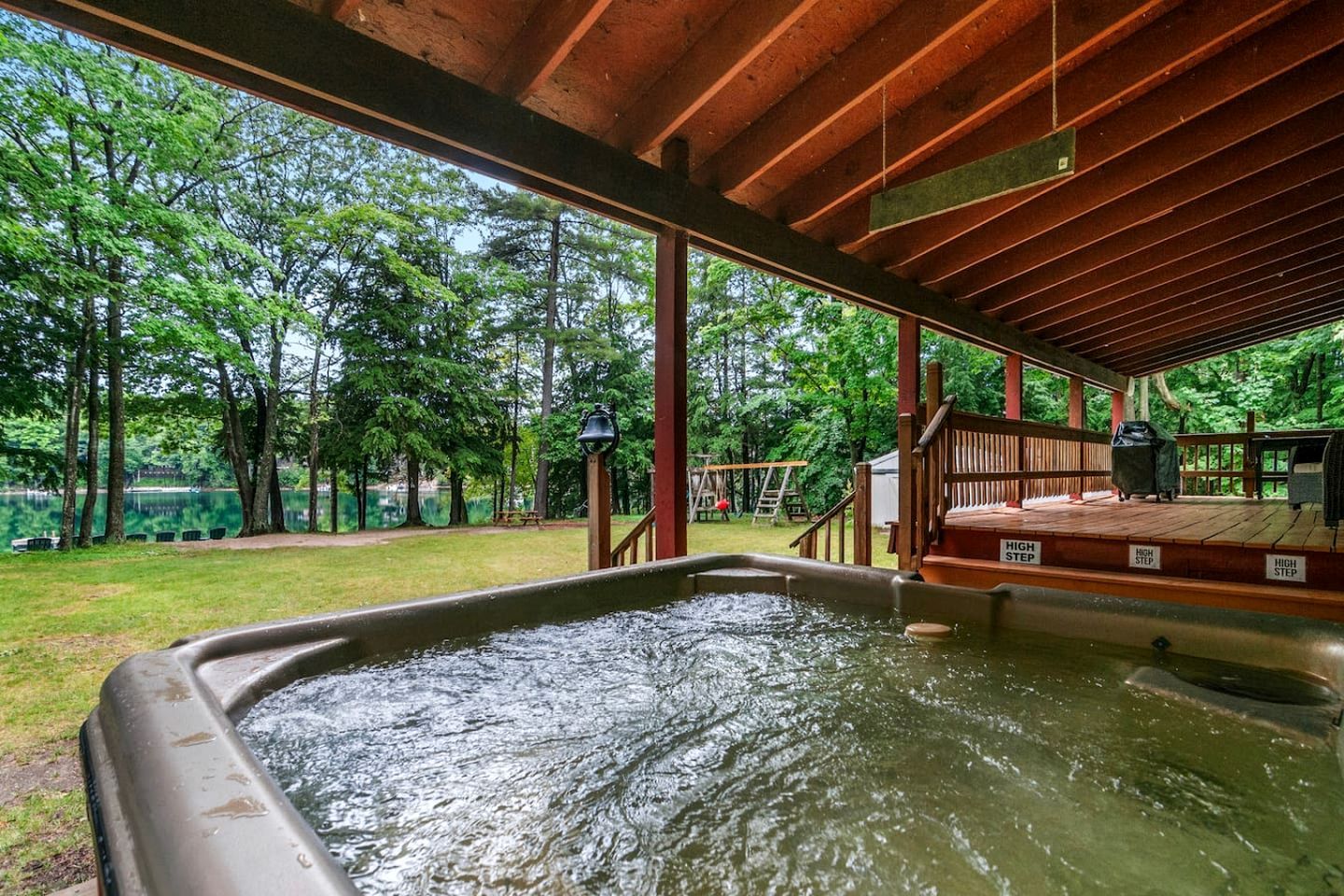 Ein Whirlpool mit Holzterrasse und Blick auf einen von Bäumen gesäumten See.