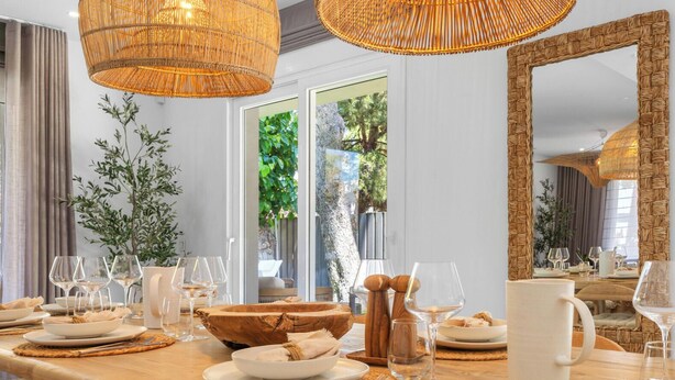 Een eetruimte met een lange houten tafel, rieten kroonluchters en een grote spiegel.