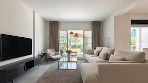 Ein modernes Wohnzimmer mit großem Flachbildfernseher, einer Couch, einem Couchtisch und einem Sessel.