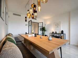 A modern dining area with a wooden table, multiple hanging pendant lights, a sofa with cushions, a plant, and a framed artwork on the wall. - Apartment 'Beachside  San-Pedro' with Mountain View, Wi-Fi and Air Conditioning (Marbella)