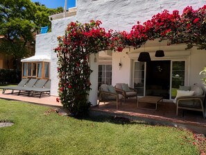 A covered outdoor seating area with lounge chairs and a table, surrounded by a white wall and red flowers. - Apartment 'Beachside  San-Pedro' with Mountain View, Wi-Fi and Air Conditioning (Marbella)