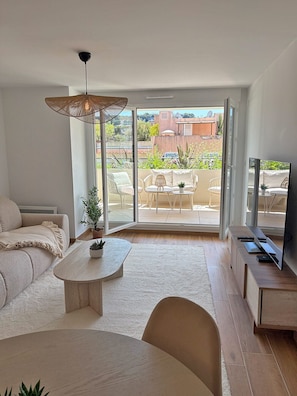 Una sala de estar moderna con un sofá, una mesa de centro, un televisor y un balcón con mobiliario de exterior.