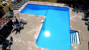 Ein rechteckiger Pool mit einer Leiter an einer Seite, umgeben von Liegestühlen und Tischen.