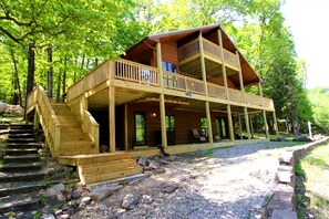 A two-story wooden cabin with a balcony, a staircase, and a covered porch area. - Nature Lover’s Dream with Expansive Tiered Deck Spaces in Garfield, Arkansas (Garfield)