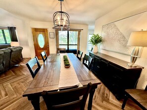 A dining area with a long wooden table, chairs, a central decorative plant, and a chandelier. - Nature Lover’s Dream with Expansive Tiered Deck Spaces in Garfield, Arkansas (Garfield)