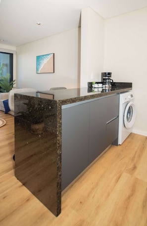 A compact kitchen with a granite countertop, a washing machine, and a coffee maker. - Corporate Stays Boggiani Flats (Asunción)