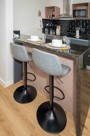 A kitchen with a bar area, two bar stools, a microwave, and a coffee machine. - Corporate Stays Boggiani Flats (Asunción)