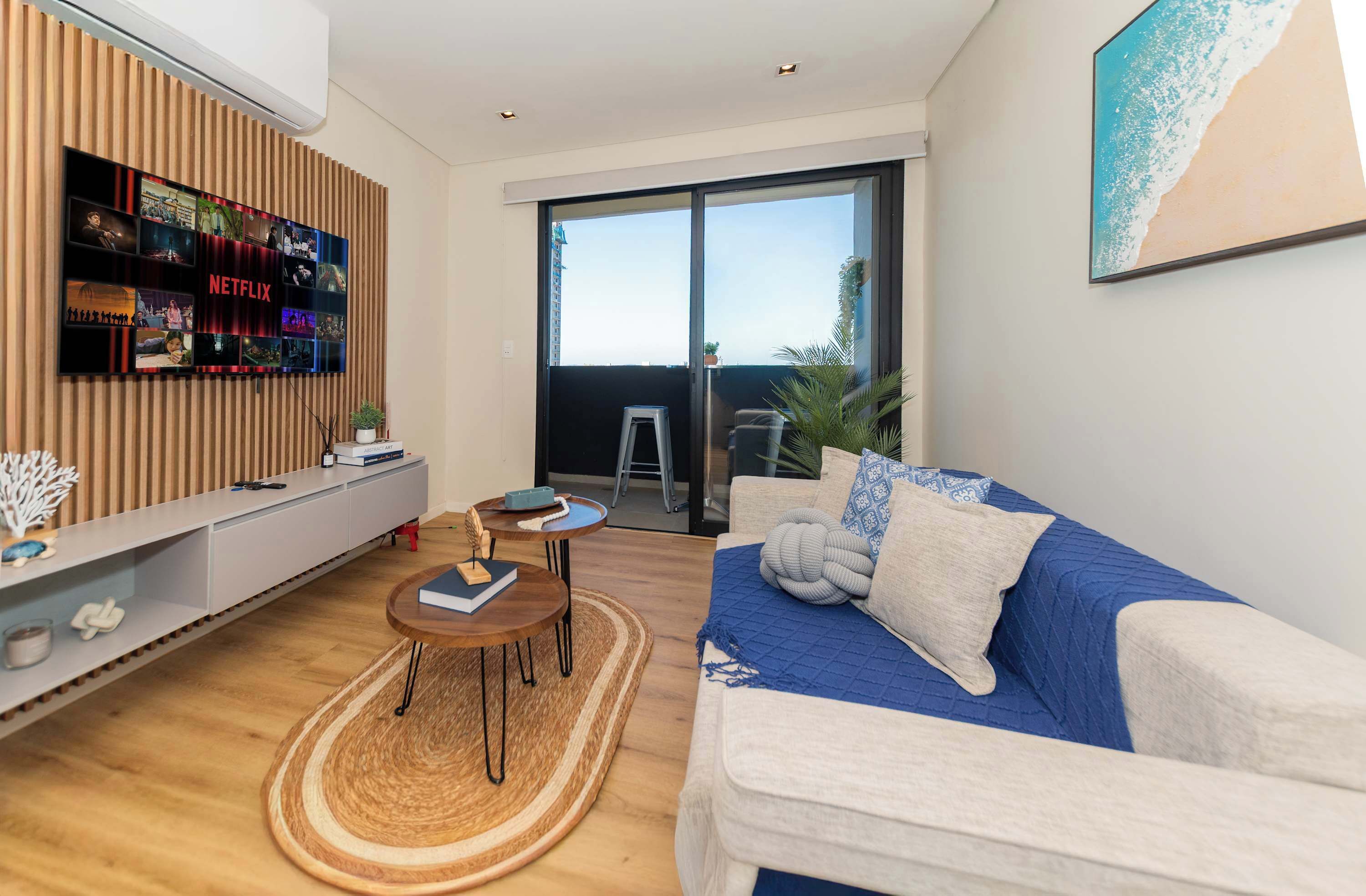 Uma sala de estar moderna com tela de exibição Netflix, um sofá, uma mesa de centro e uma porta de vidro deslizante que dá para uma varanda.