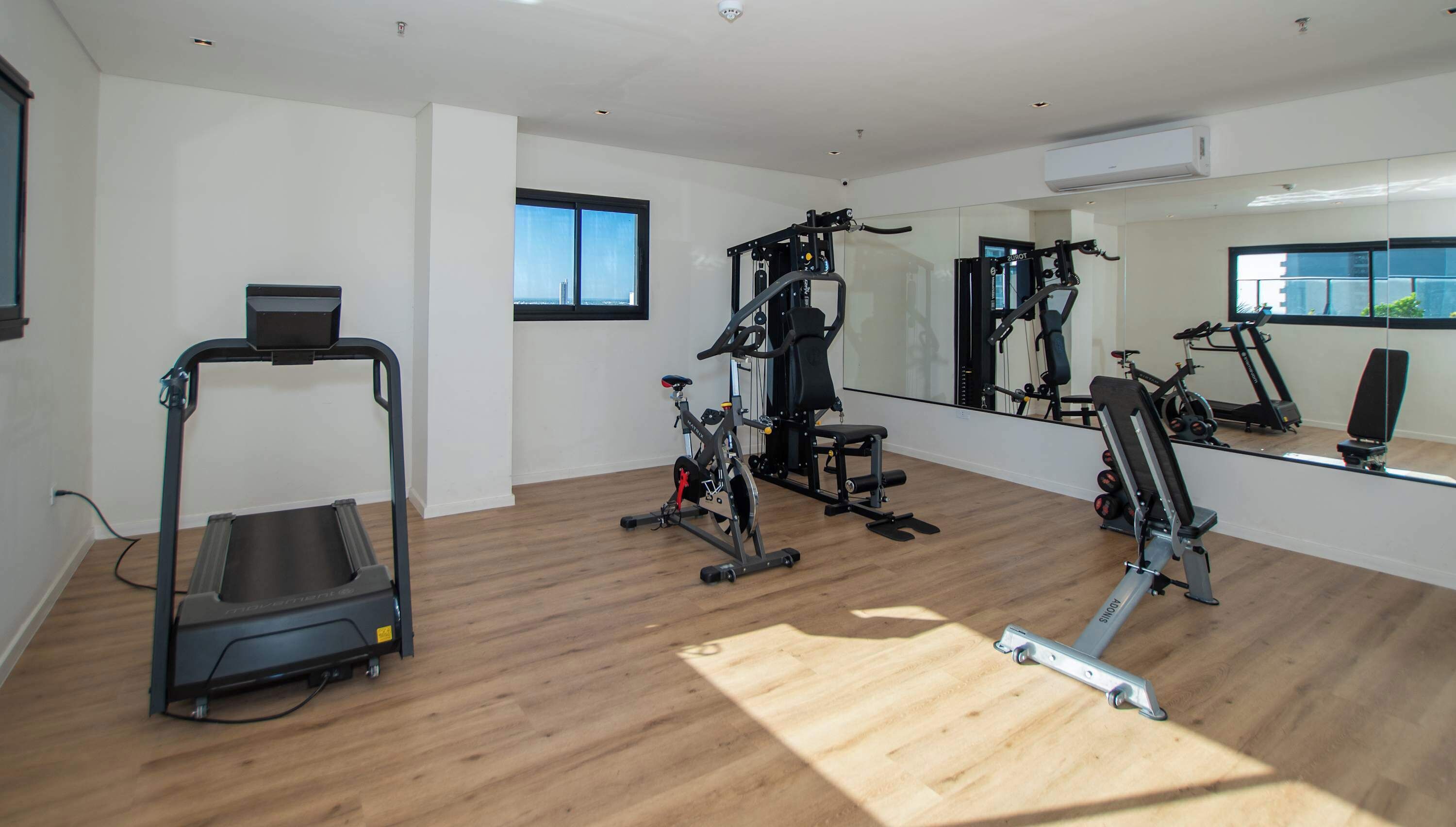 Un gimnasio con cinta de correr, bicicletas estáticas y máquinas de pesas.