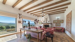 A spacious living room with a large window, a fireplace, and a view of the countryside. - Charming and Spacious Family Villa - Cortijo Sierra y Lago (Arcos de la Frontera)