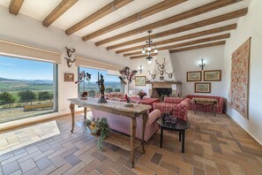 A spacious living room with a large window, a fireplace, and a view of the countryside. - Charming and Spacious Family Villa - Cortijo Sierra y Lago (Arcos de la Frontera)
