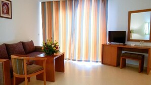 Uma sala de estar com sofá, mesa de centro, televisão e escrivaninha com espelho.