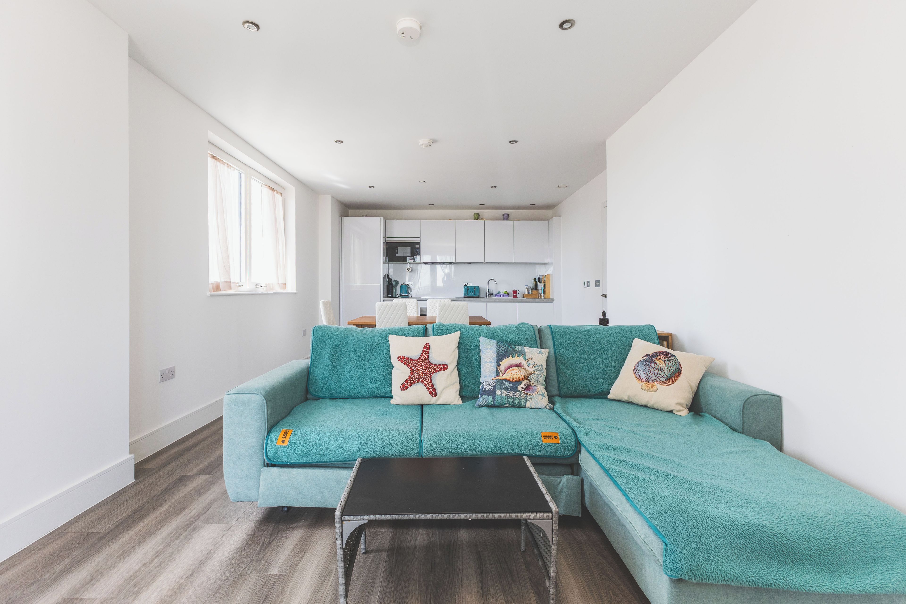 A modern living room with a teal sofa, a black coffee table, and decorative pillows.