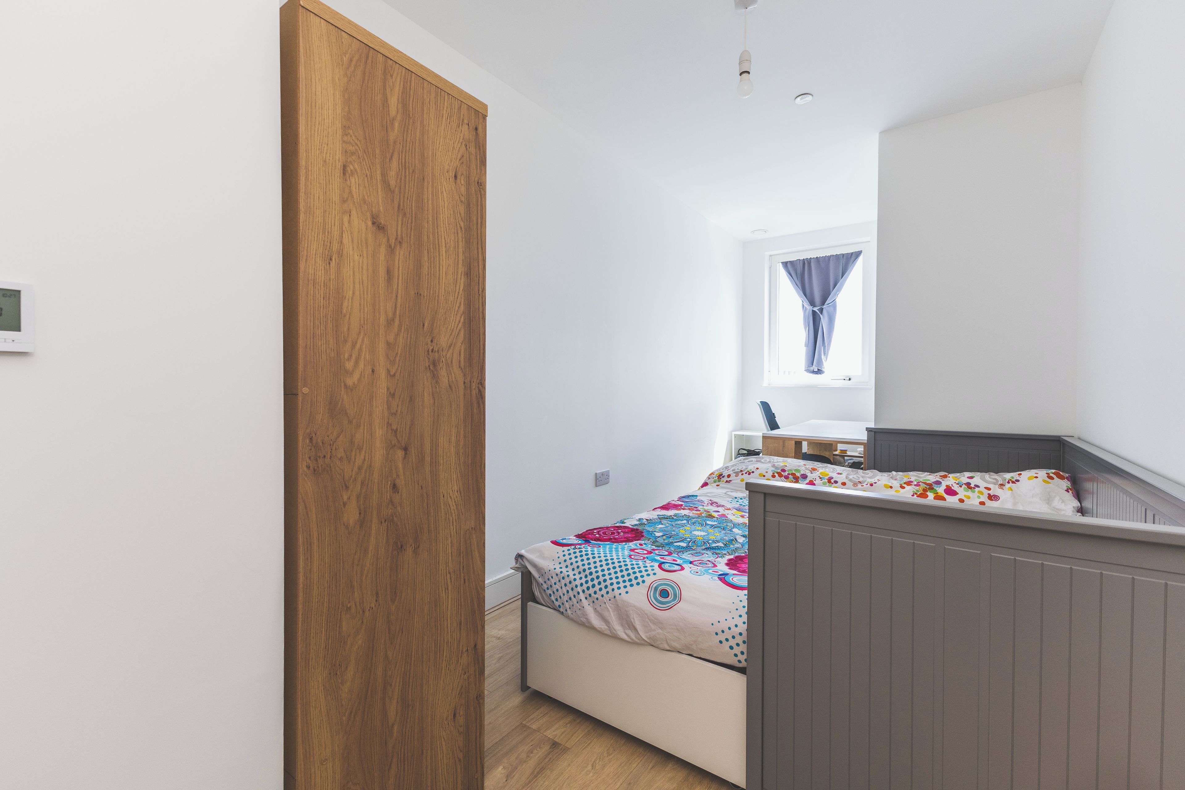 Une chambre à coucher avec un lit, une armoire en bois, une fenêtre avec des rideaux et un bureau avec une chaise.