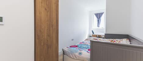 Une chambre à coucher avec un lit, une armoire en bois, une fenêtre avec des rideaux et un bureau avec une chaise.