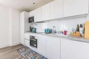 A modern kitchen with white cabinets, a microwave, a toaster, and a sink. - Modern 1BDR Flat Near Elizabeth Line and Heathrow (Greater London)