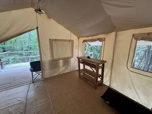 Ein Zelt mit Holztisch, einem schwarzen Stuhl und Fenstern mit Blick auf den Wald.