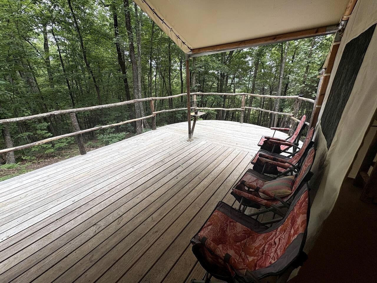 Une terrasse en bois dotée d’un espace salon couvert, entourée d’une barrière en corde, et offrant une vue sur une zone boisée.
