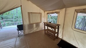 Une tente avec une table en bois, une chaise noire et des fenêtres donnant sur la forêt.