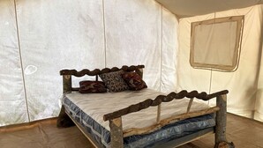 Un lit doté d’une structure en bois rustique et d’un matelas, le tout installé dans une pièce qui ressemble à une tente.