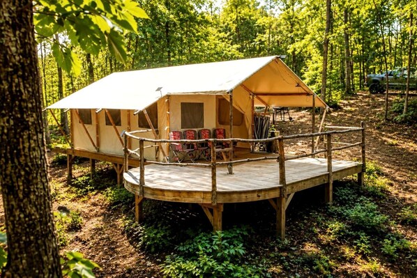 A forested campsite with a single tent, a wooden deck, and seating.
