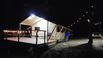 A tented structure with a covered seating area and a small stage, surrounded by string lights.