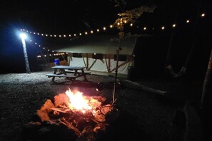 Ein Lagerfeuer mit Picknicktisch und Lichterketten auf einem Campingplatz.