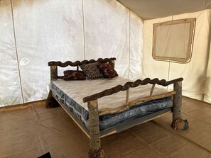 A bed with a rustic wooden frame and a mattress in a tent-like room.