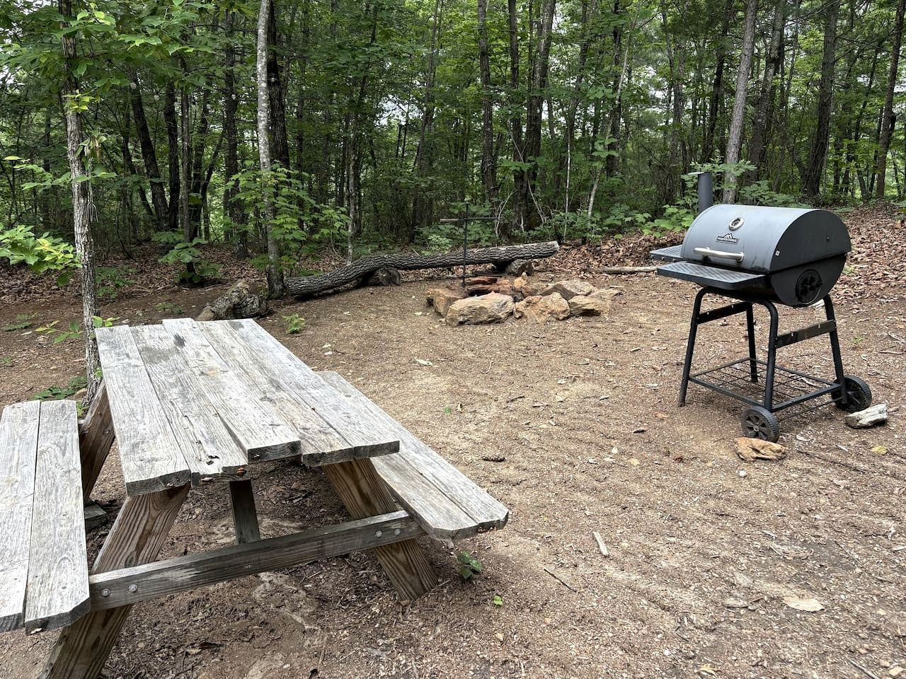 A picnic table and a portable grill in a forested area.
