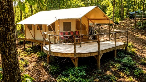Un terrain de camping boisé avec une seule tente, une terrasse en bois et des sièges.