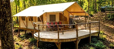 A forested campsite with a single tent, a wooden deck, and seating.