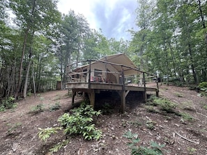 A wooden cabin with a deck, surrounded by a forest.