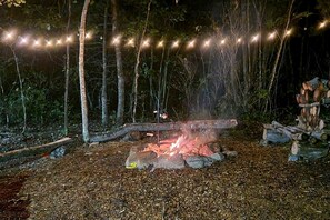A campfire surrounded by logs and a string of lights in a wooded area.
