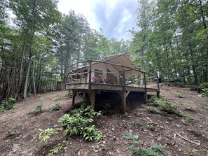 A wooden cabin with a deck, surrounded by a forest.
