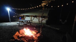 Un feu de camp avec une table de pique-nique et des guirlandes lumineuses, le tout installé dans un cadre de camping.