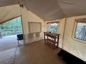 A tent with a wooden table, a black chair, and windows with forest views.