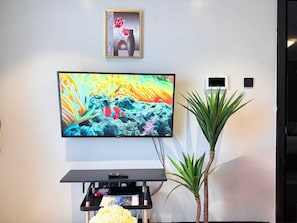Ein Flachbildfernseher an der Wand, darüber ein kleines gerahmtes Bild und daneben eine Topfpflanze.