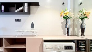 A compact laundry area with a washing machine, shelves with storage containers, and a small ironing station. - Nairobi, Kenya. Spacious & Elegant studio Apartment +Gym+Pool+Rooftop Restaurant (Nairobi)