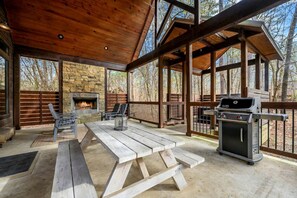 Une terrasse couverte avec une cheminée en pierre, un barbecue et des sièges.