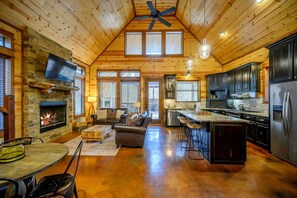 A spacious log cabin interior with a fireplace, a living area with a sofa and coffee table, a kitchen with modern appliances, and large windows allowing natural light. - Luxury Cabin with Hot Tub & Game Room Retreat in Broken Bow, Oklahoma (Broken Bow)