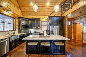 A kitchen with dark cabinets, a central island with stools, stainless steel appliances, and wooden ceiling beams. - Luxury Cabin with Hot Tub & Game Room Retreat in Broken Bow, Oklahoma (Broken Bow)